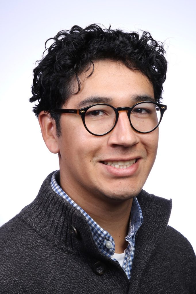Head and shoulders portrait of Isaiah Jimenez in a grey sweater and blue checked shirt.